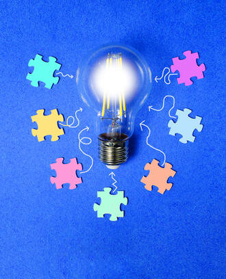 A lightbulb is surrounded by various colorful puzzle pieces